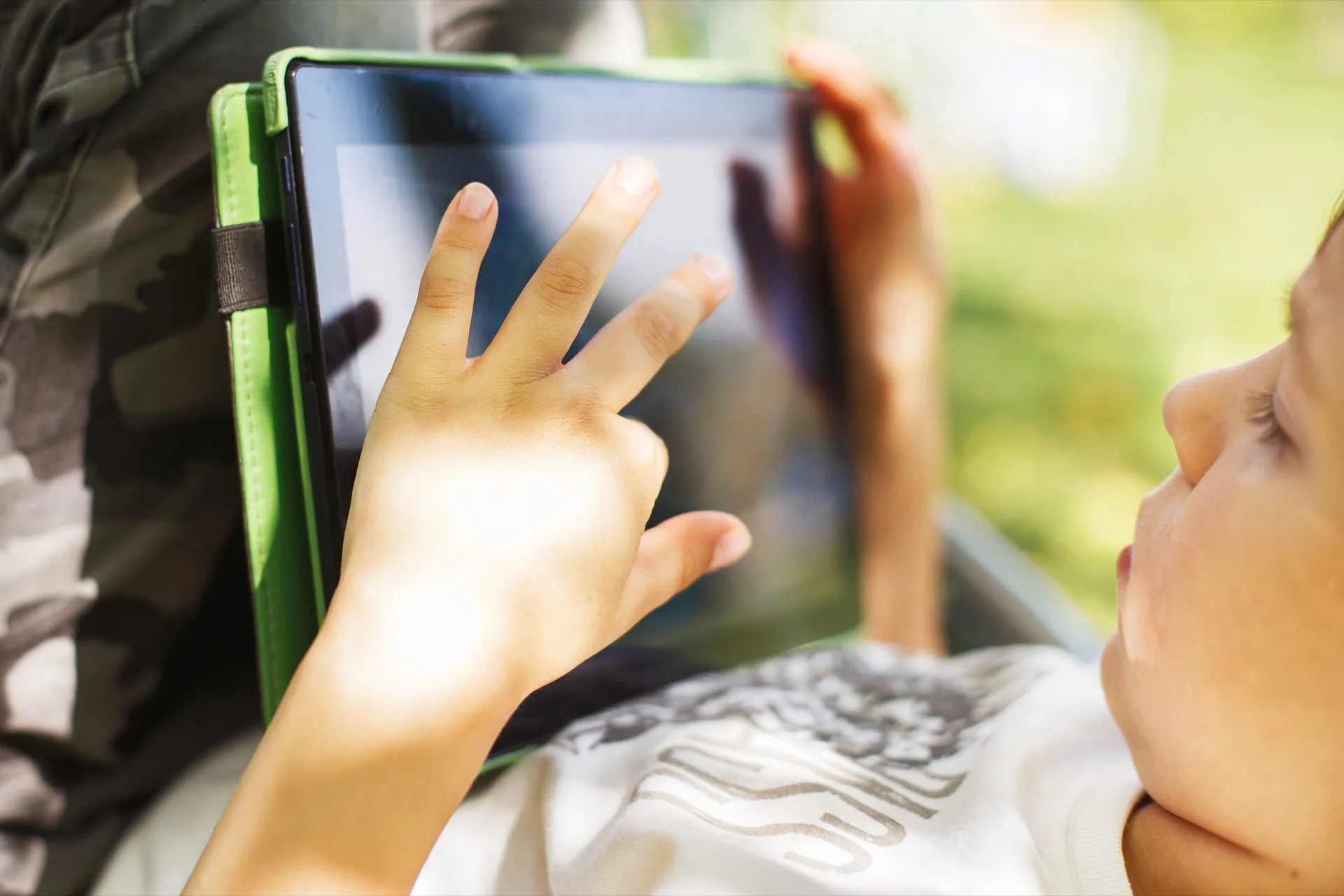 A child's hand on a tablet screen outdoors